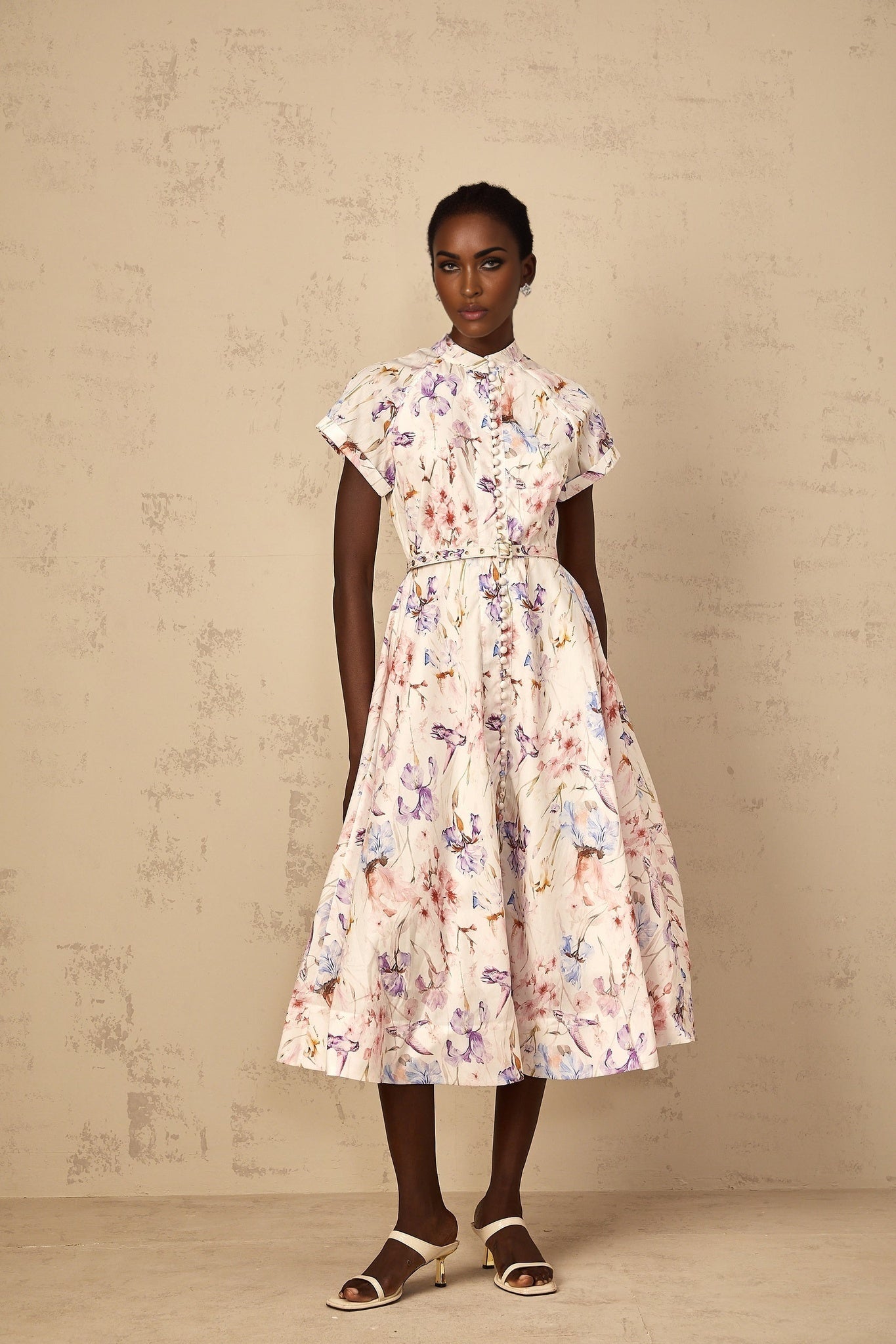 A white floral print midi dress with a mock neck worn by a woman standing against a plain background