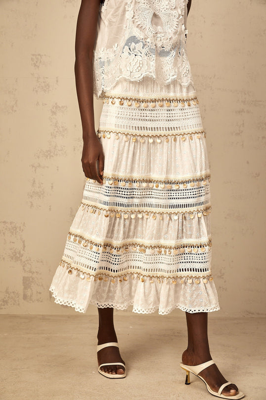 A white flowy midi skirt with shirred waistband and bohemian style pattern worn by a model against a plain background