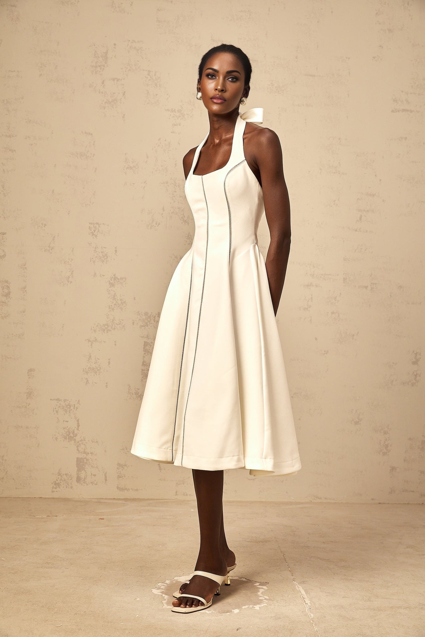 A white halterneck midi dress with a bow detail at the neckline featuring a fitted bodice and flowy skirt