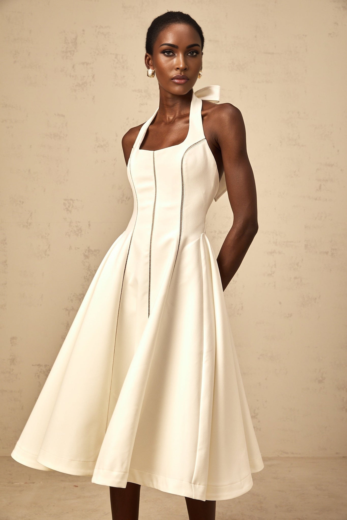 A white halterneck midi dress with a bow detail at the neckline featuring a fitted bodice and flowy skirt