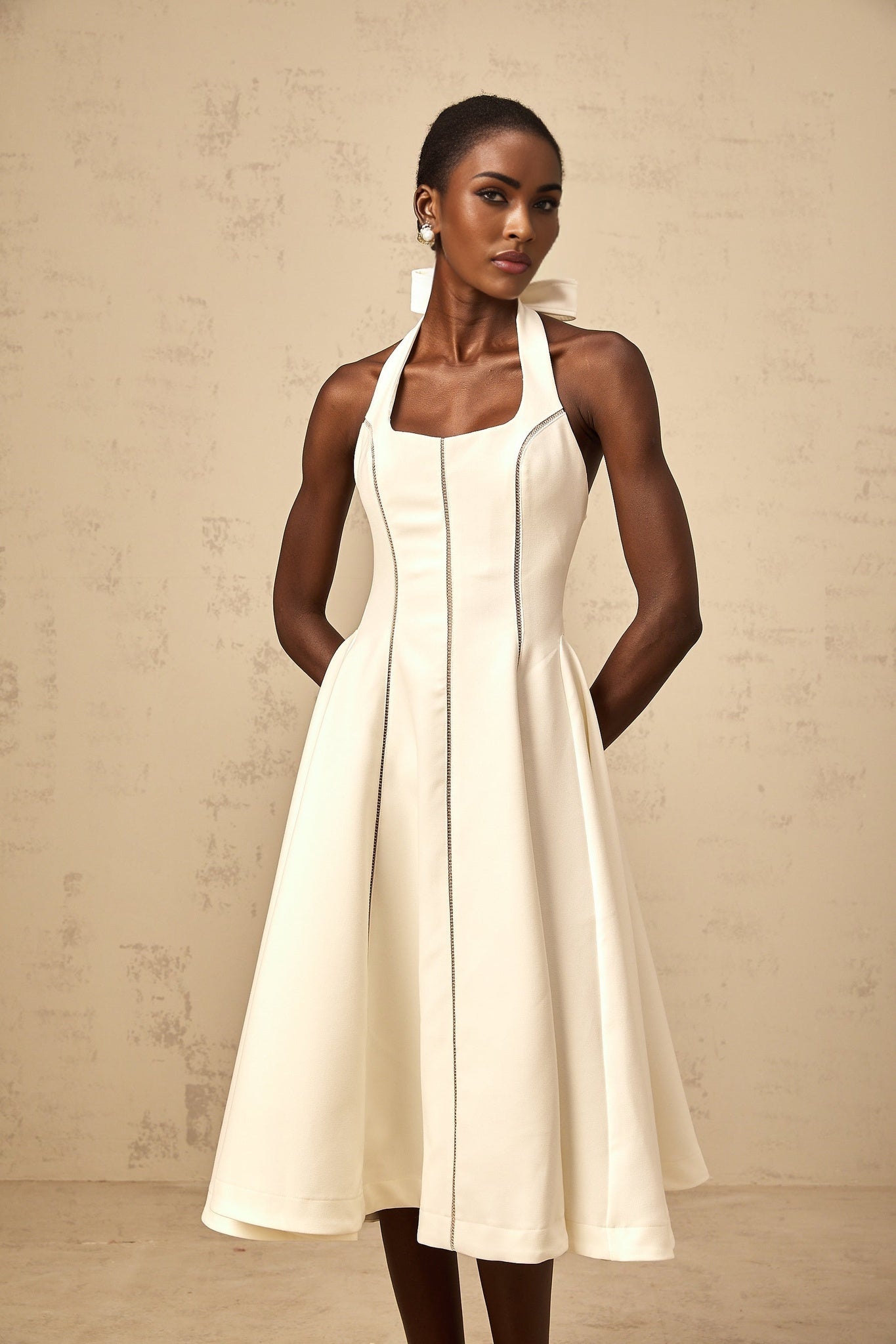 A white halterneck midi dress with a bow detail featuring a fitted bodice and flared skirt