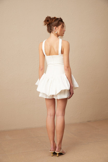 A white halterneck mini dress with ruffled details called Olivia worn by a female model against a plain background
