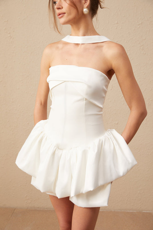 A white halterneck mini dress with ruffled details worn by a model named Olivia standing against a plain background