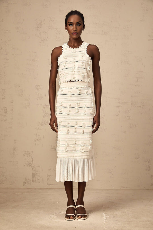 A white knit matching set consisting of a top and skirt with pointelle trim detailing Paola brand clothing displayed on a plain background