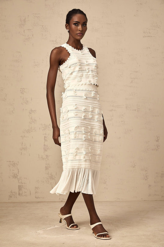A white knit twopiece outfit consisting of a top and skirt with pointelle trim details The top is sleeveless and the skirt is kneelength Both pieces feature a textured knit pattern and delicate eyelet designs along the edges