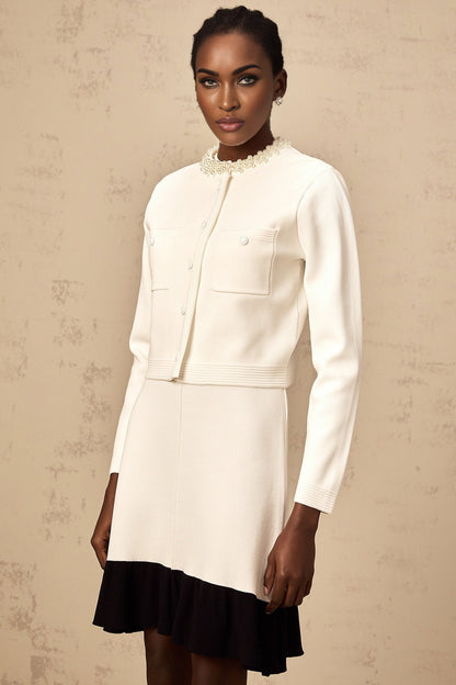 A white knitted cardigan adorned with faux pearl embellishments featuring a classic design and button front closure