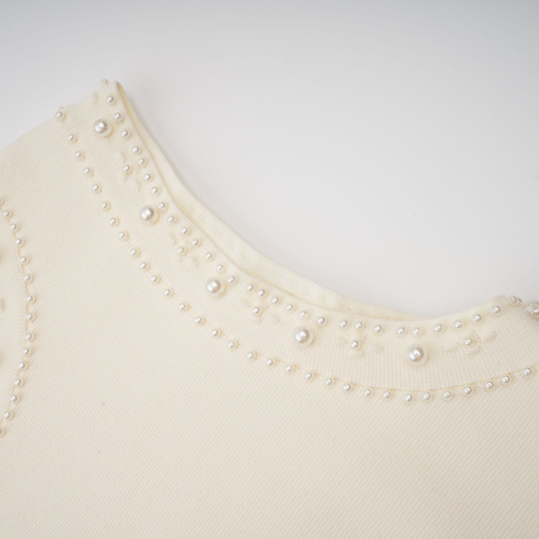 A white knitted maxi dress with faux pearl embellishments worn by a model standing against a plain background