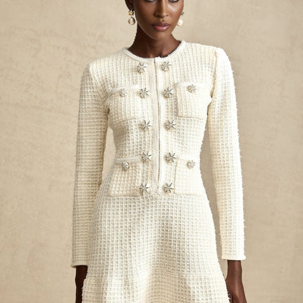 A white knitted mini dress with a flared skirt and short sleeves on a female model against a plain background