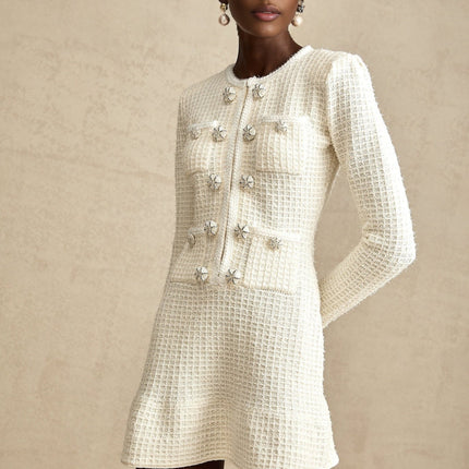 A white knitted mini dress with a flared skirt and short sleeves on a model against a plain background