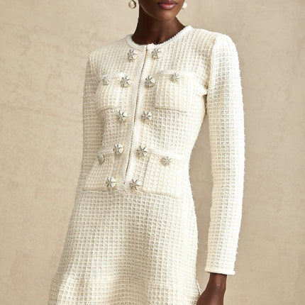 A white knitted mini dress with a flared skirt and short sleeves worn by a model standing against a plain background
