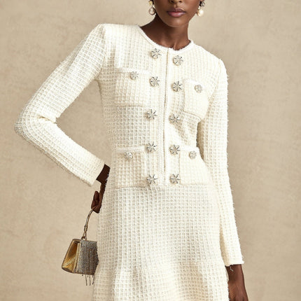 A white knitted mini dress with a flared skirt design named Liane worn by a model against a plain background