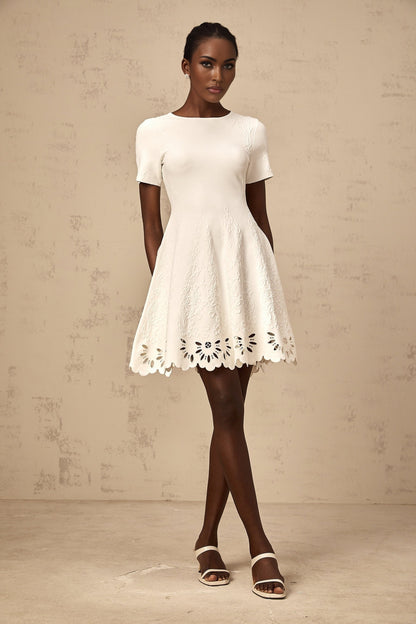 A white knitted mini dress with cut out jacquard detailing worn by a model named Emilie
