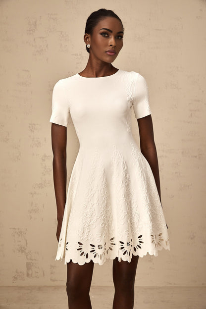 A white knitted mini dress with cut out jacquard pattern featuring a short hemline and intricate textured design