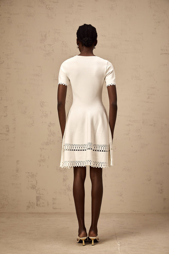 A white knitted mini dress with cutout details featuring a fitted silhouette and short length