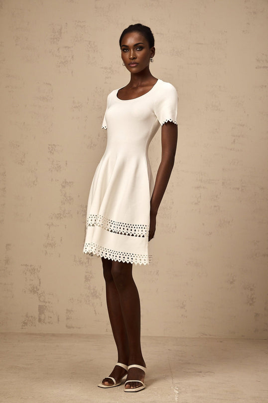 A white knitted mini dress with cutout details featuring a fleur design pattern short length and form fitting silhouette