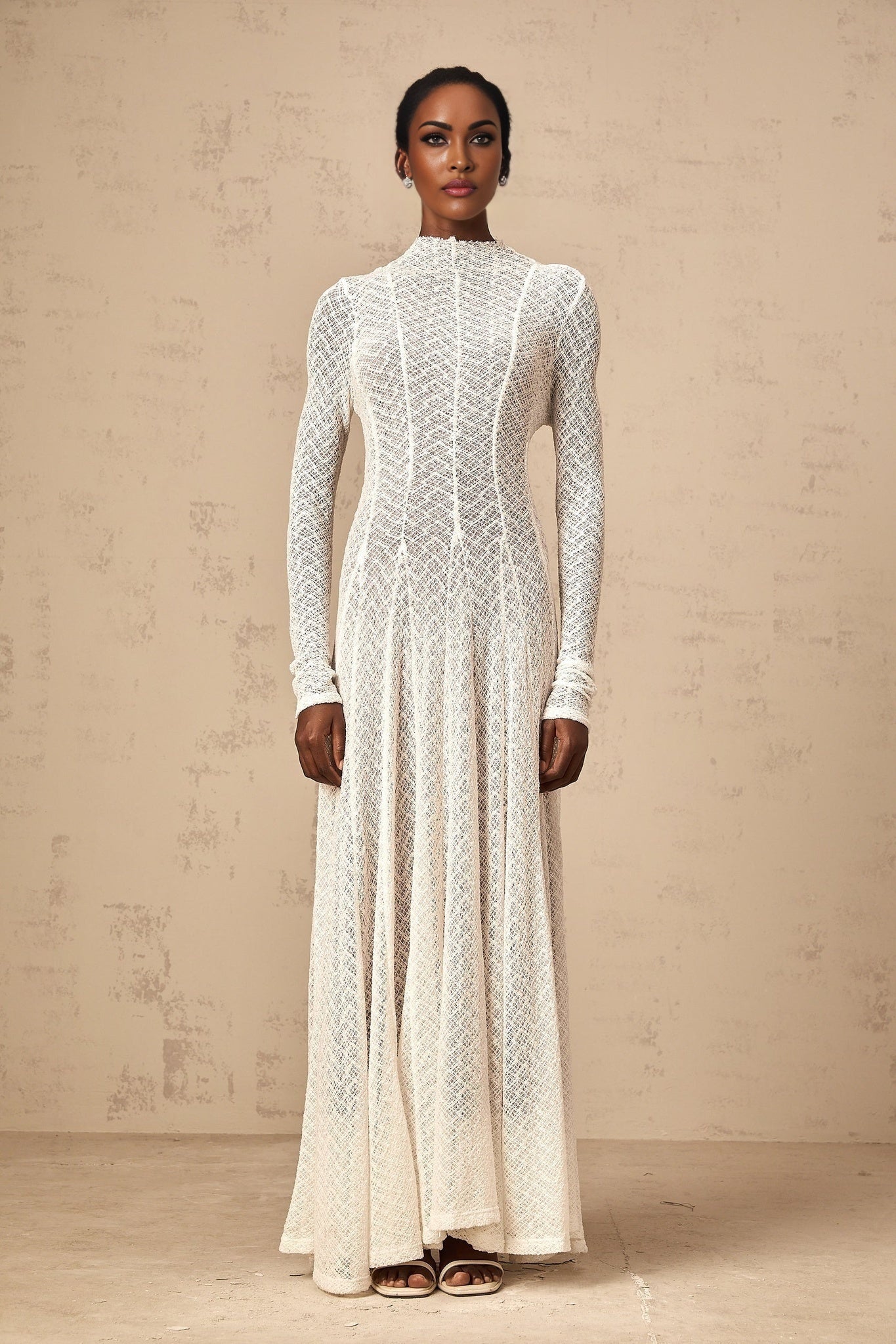 A white lace maxi dress with a wavy pattern design featuring long sleeves and a flowing skirt