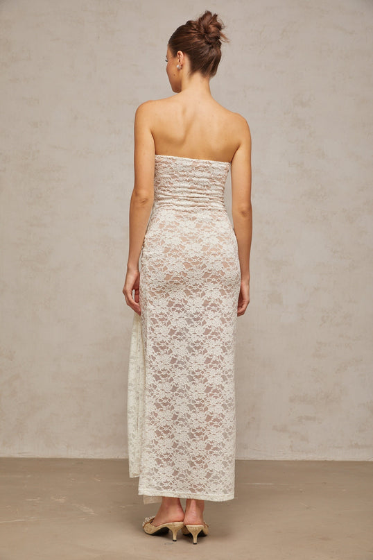 A white lace midi dress with draped detailing named Wilhelmine worn by a model standing against a plain background
