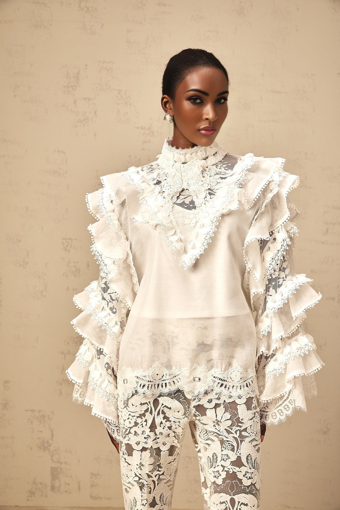 A white layered lace blouse with a tied neckline featuring delicate floral patterns and ruffled details