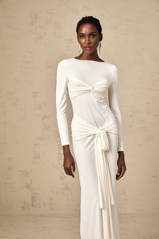 A white long maxi dress with ruched fabric and a twisted ribbon detail at the waist named Elena