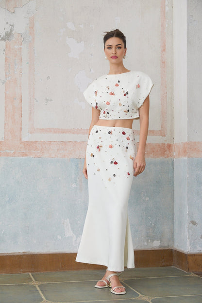 A white matching set consisting of a top and skirt adorned with shell embellishments featuring a design inspired by Delphine