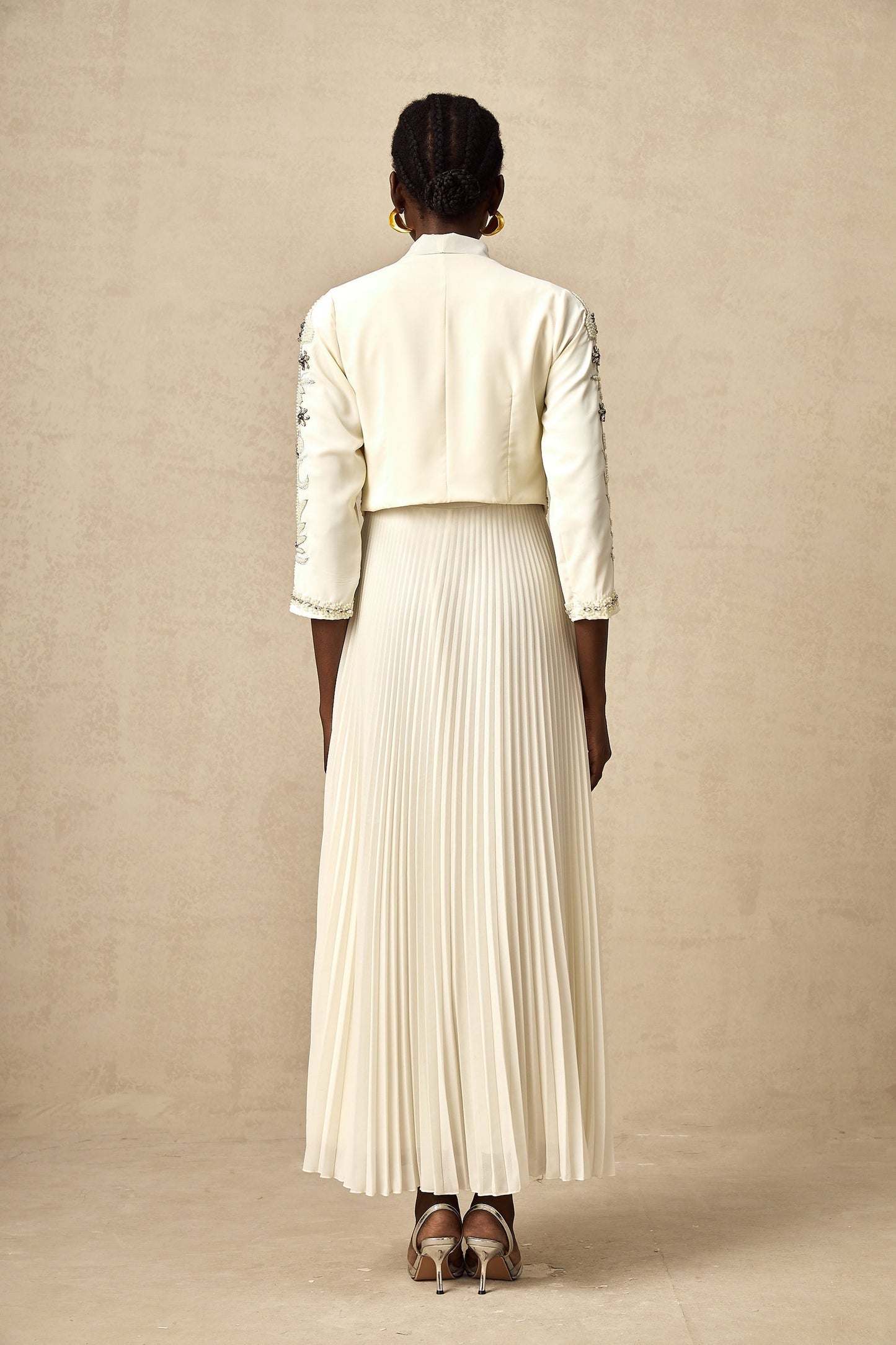 A white matching set featuring a pleated jacket and dress with embellished details The jacket has a structured silhouette while the dress is fitted Both pieces are adorned with delicate embellishments for an elegant look