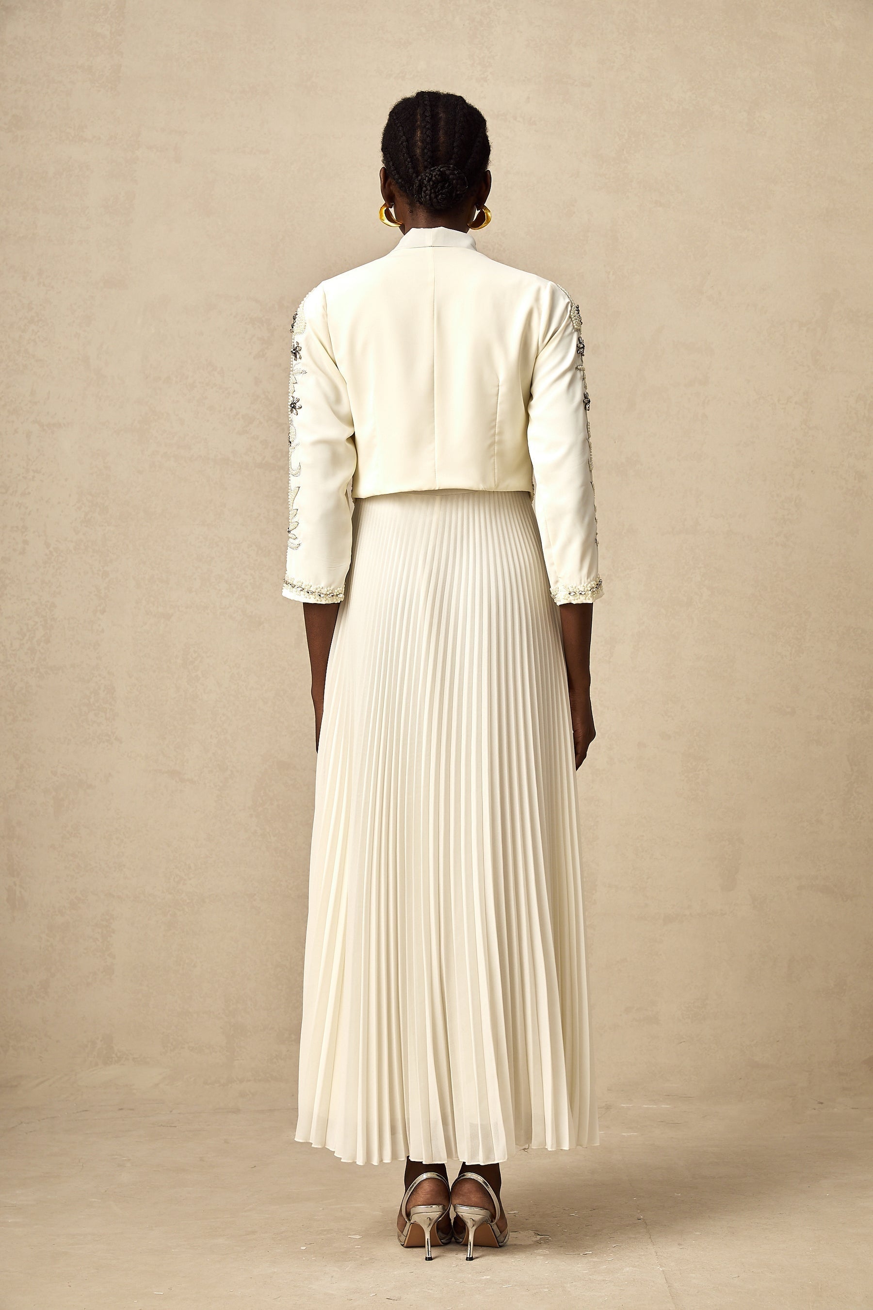 A white matching set featuring a pleated jacket and dress with embellished details The jacket has a structured silhouette while the dress is fitted Both pieces are adorned with delicate embellishments for an elegant look