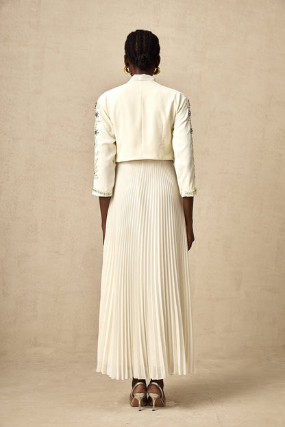 A white matching set featuring a pleated jacket and dress with embellished details The jacket has a structured silhouette while the dress is fitted Both pieces are adorned with delicate embellishments for an elegant look
