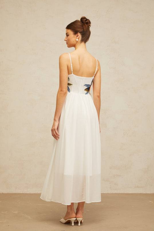 A white maxi dress with floral embroidery and shirred detailing named Josette