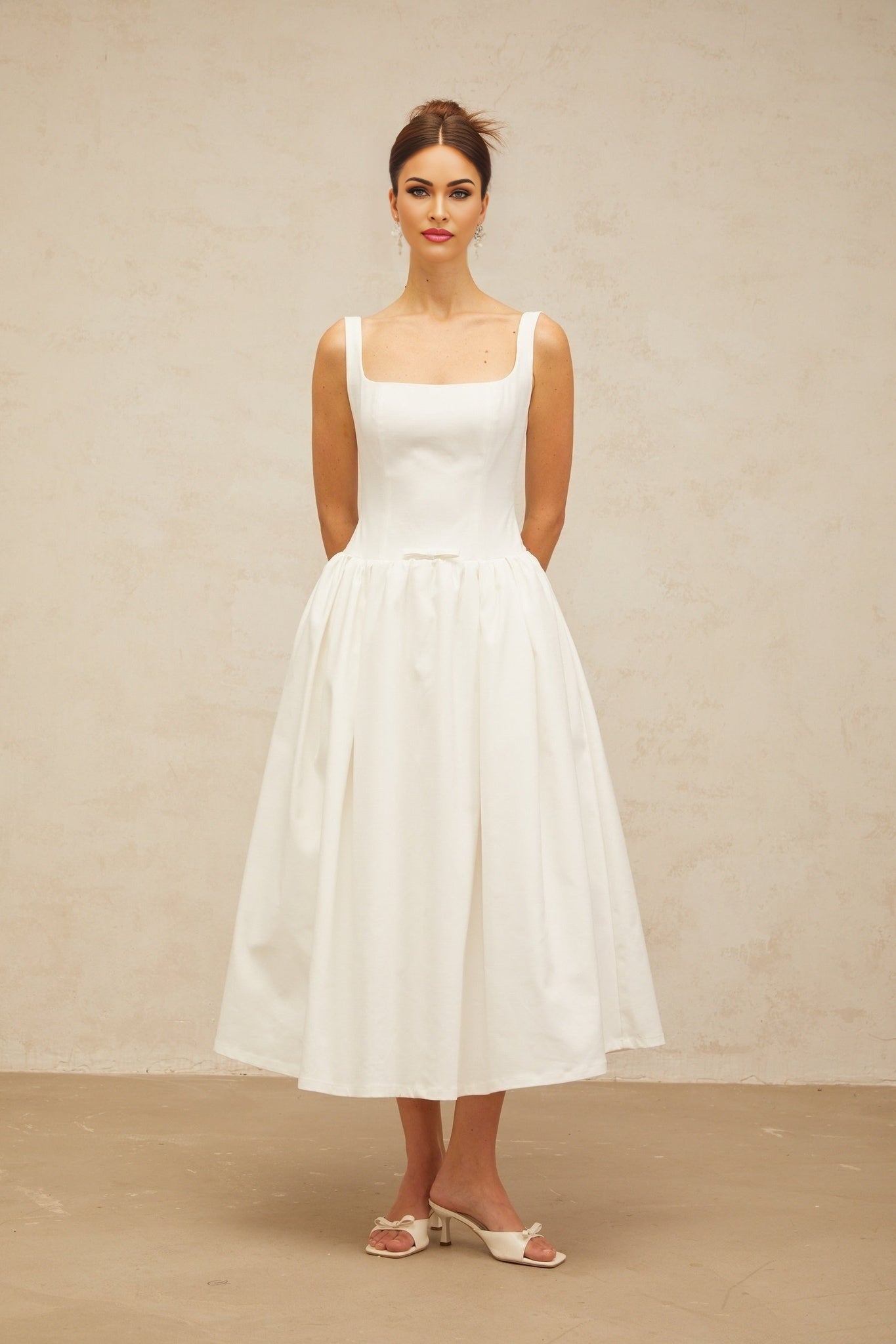 A white midi dress with a bowknot detail and flounced design featuring a feminine silhouette and delicate ruffles
