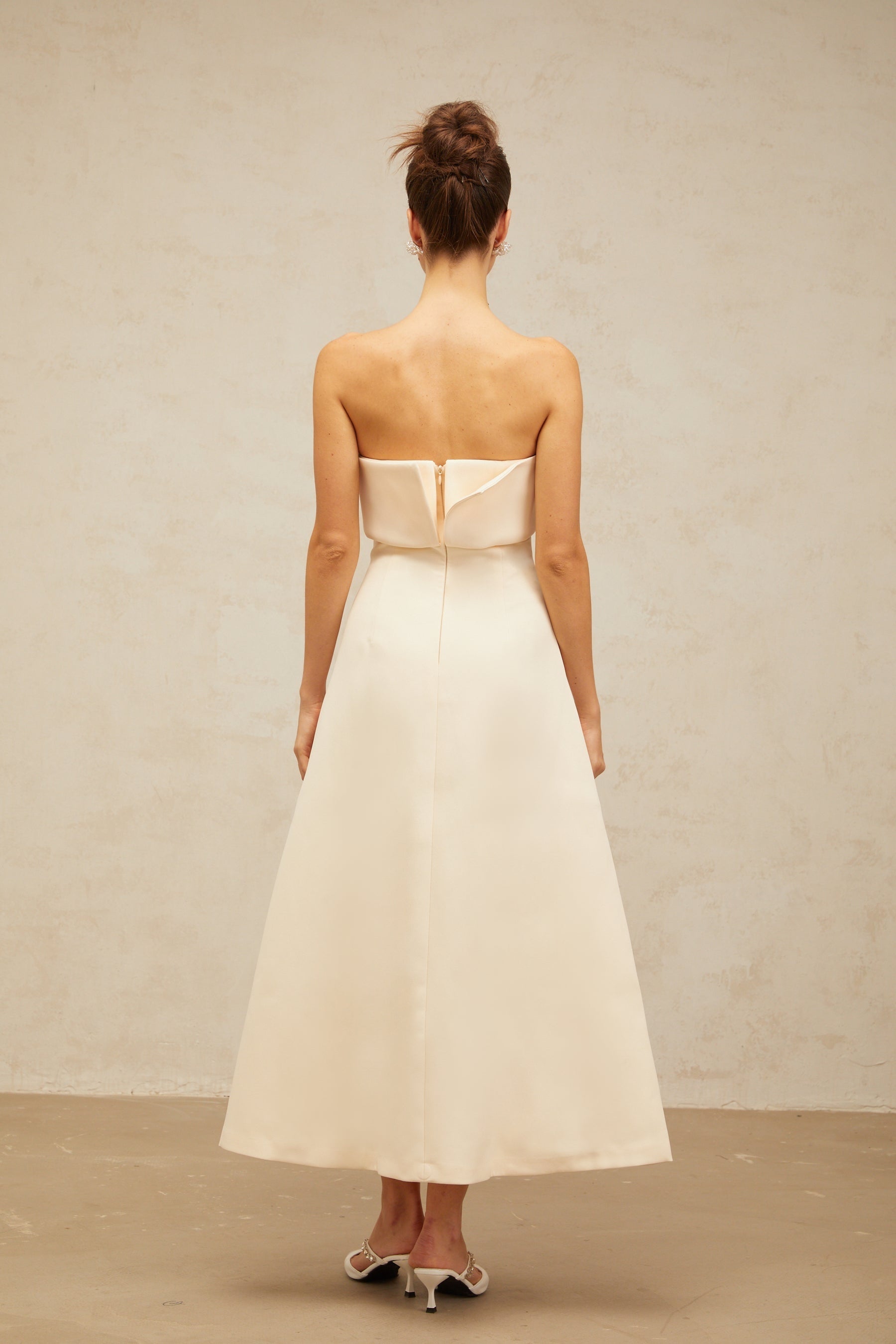 A white midi dress with a corsetstyle bodice and folded details worn by a model standing against a plain background
