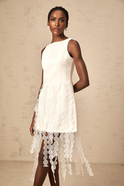 A white midi dress with a discshaped design and fringe details modeled by a woman named Justine