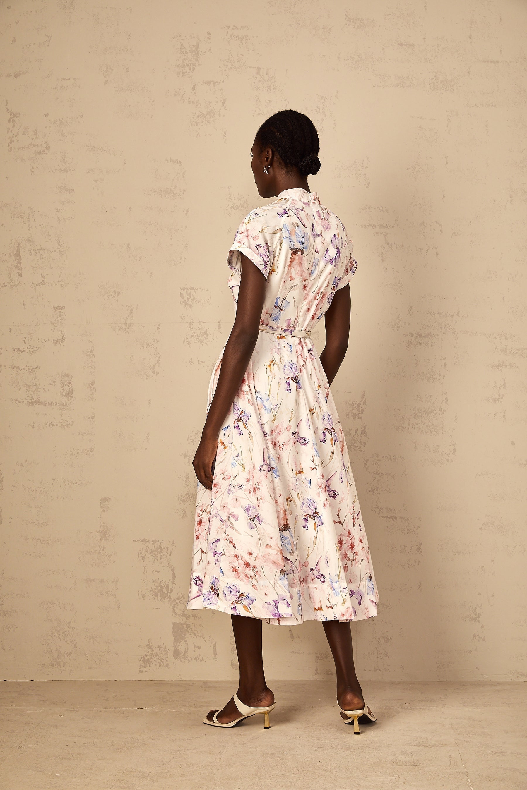 A white midi dress with a floral print and mock neck worn by a woman standing in a neutral setting