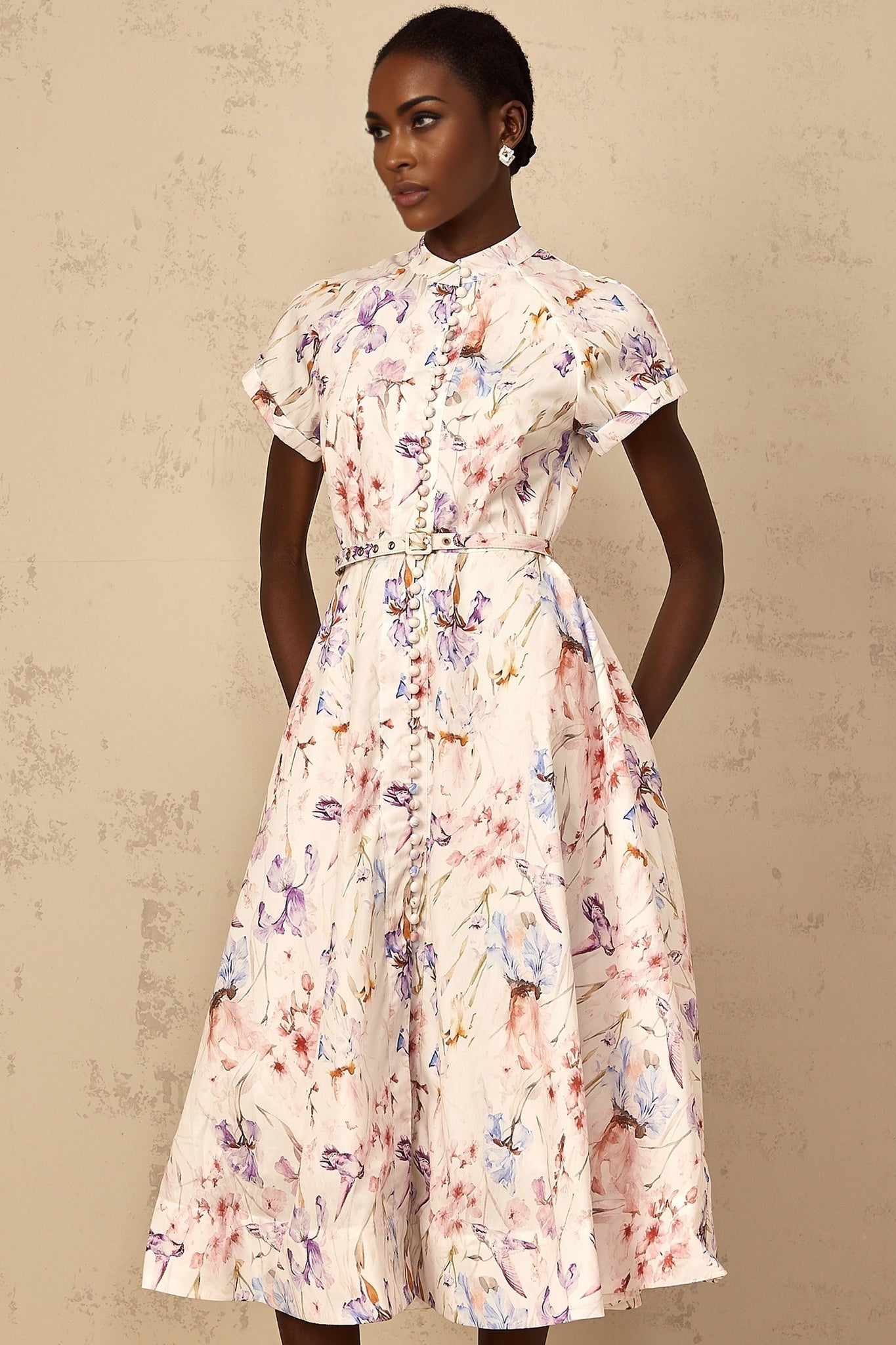 A white midi dress with a floral print and mock neckline worn by a woman standing in a neutral background