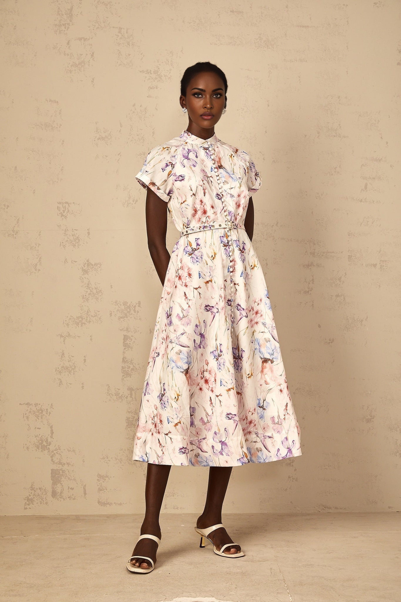 A white midi dress with a mock neck and floral print pattern worn by a woman standing in a neutral background
