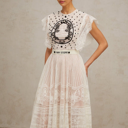 A white midi dress with a pleated skirt featuring jacquard floral lace pattern and called Phoebe