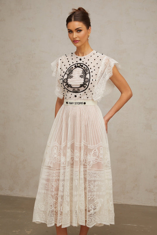 A white midi dress with a pleated skirt featuring jacquard floral lace pattern and called Phoebe