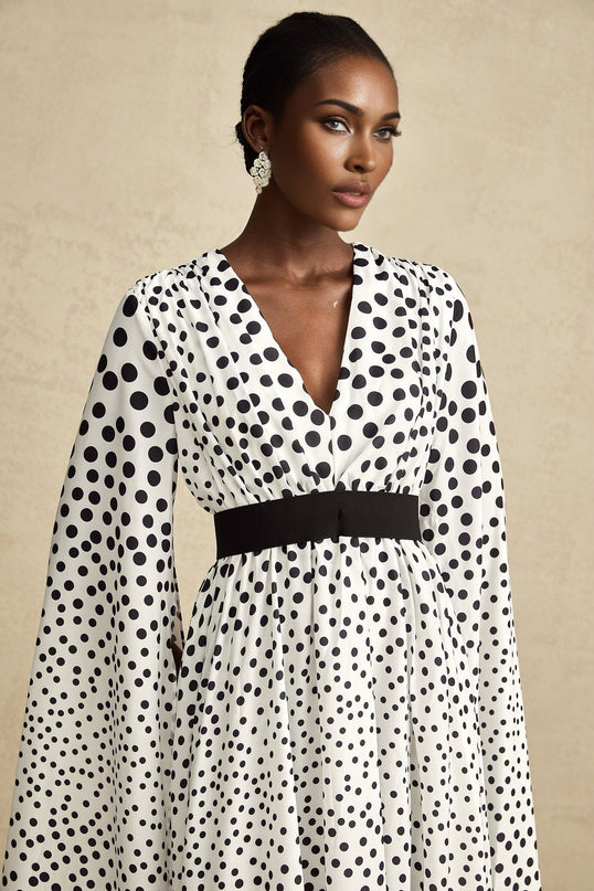 A white midi dress with black polka dots featuring slit sleeves and a feminine silhouette