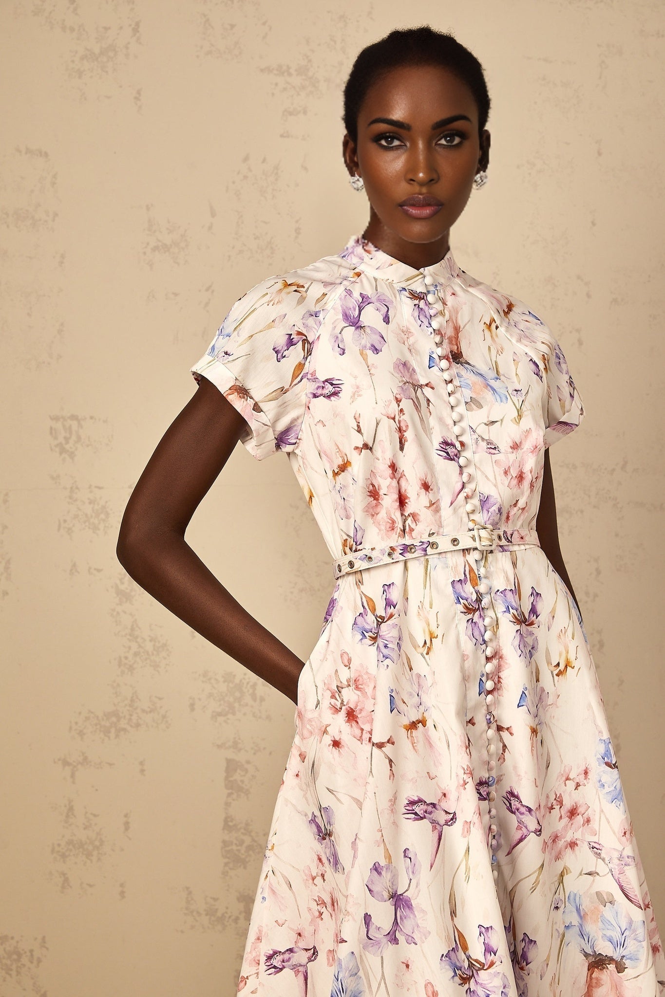 A white midi dress with floral print and mock neck design worn by a woman standing in a neutral setting
