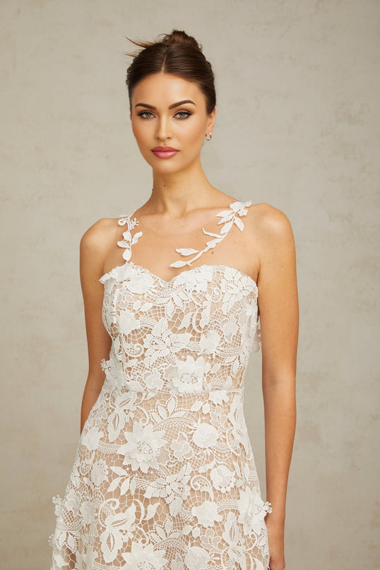 A white midi dress with lace detailing and tulle panels worn by a model standing against a plain background