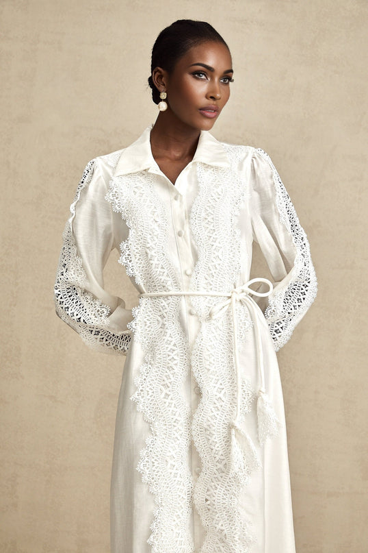 A white midi dress with lace details and a tied waist featuring a feminine silhouette and delicate design elements