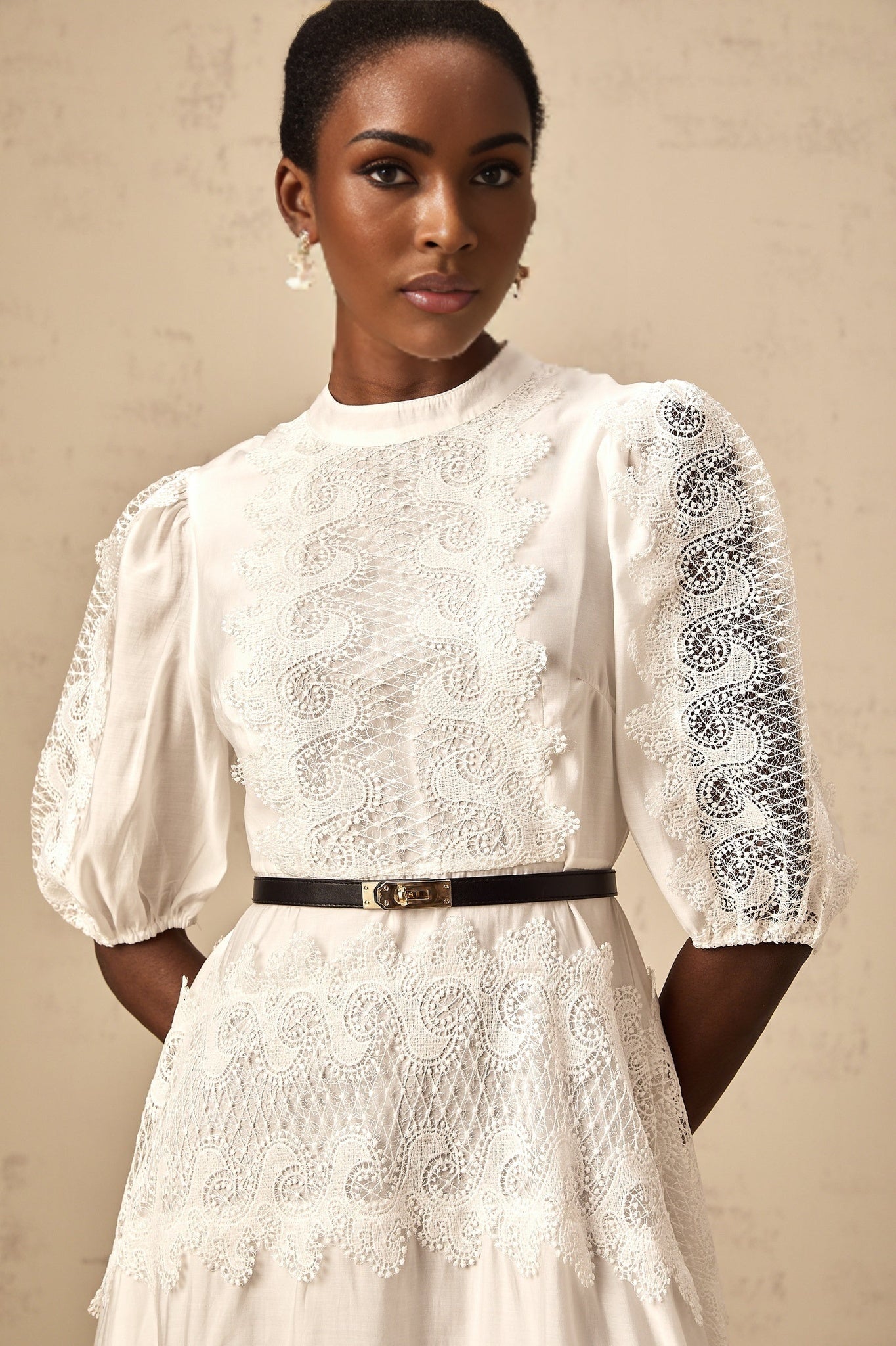 A white midi dress with lace trim panels and a belt at the waist featuring a slim fit and delicate feminine design