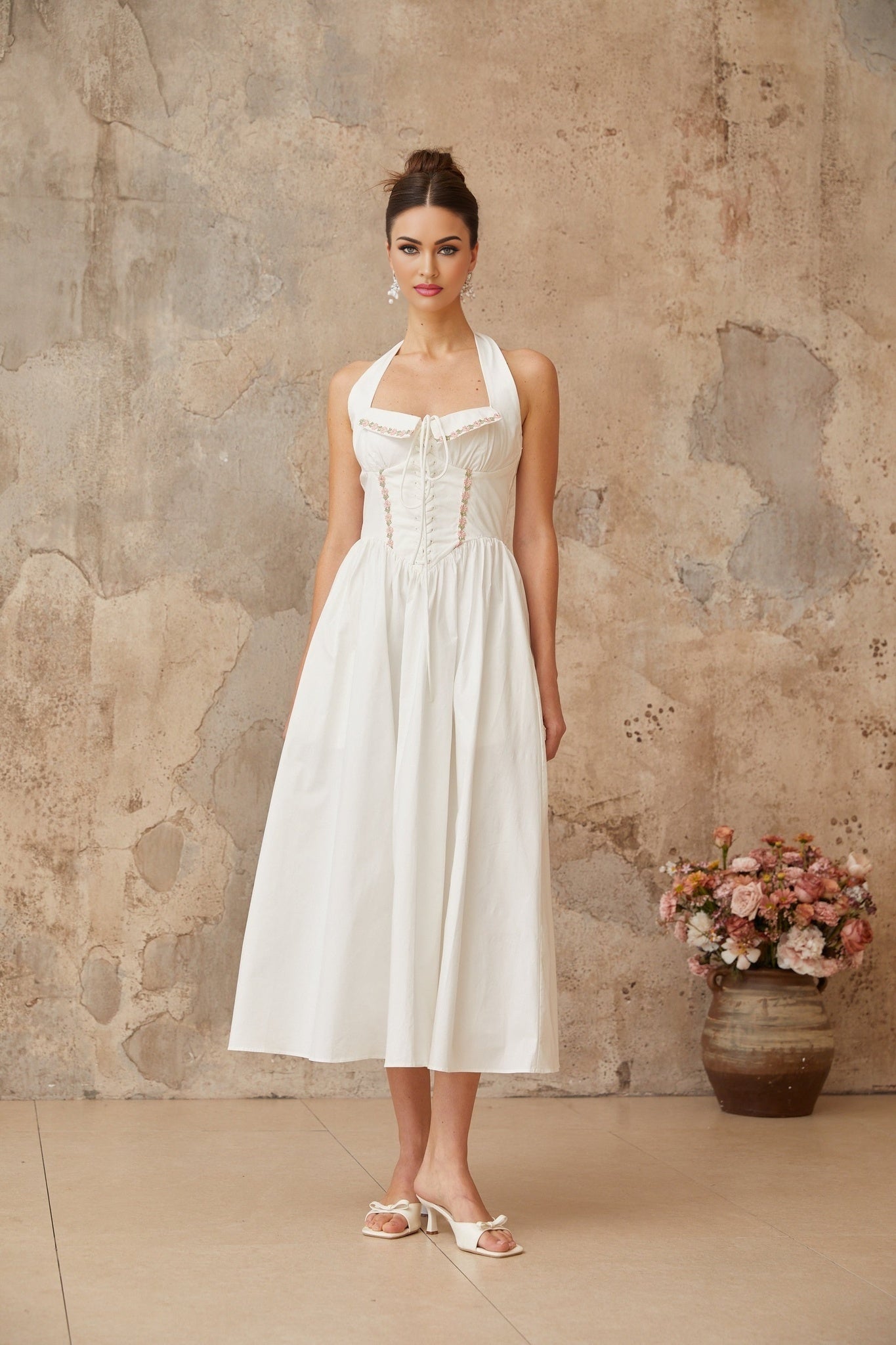 A white midi dress with laceup detail and shirred fabric featuring a feminine silhouette and delicate design elements