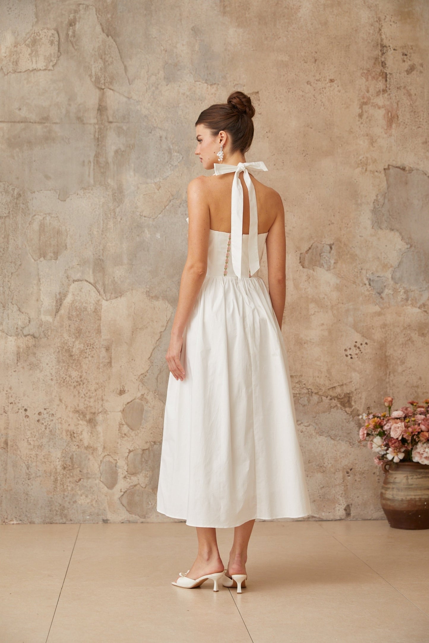 A white midi dress with laceup detailing and shirred fabric featuring a feminine silhouette and delicate design elements