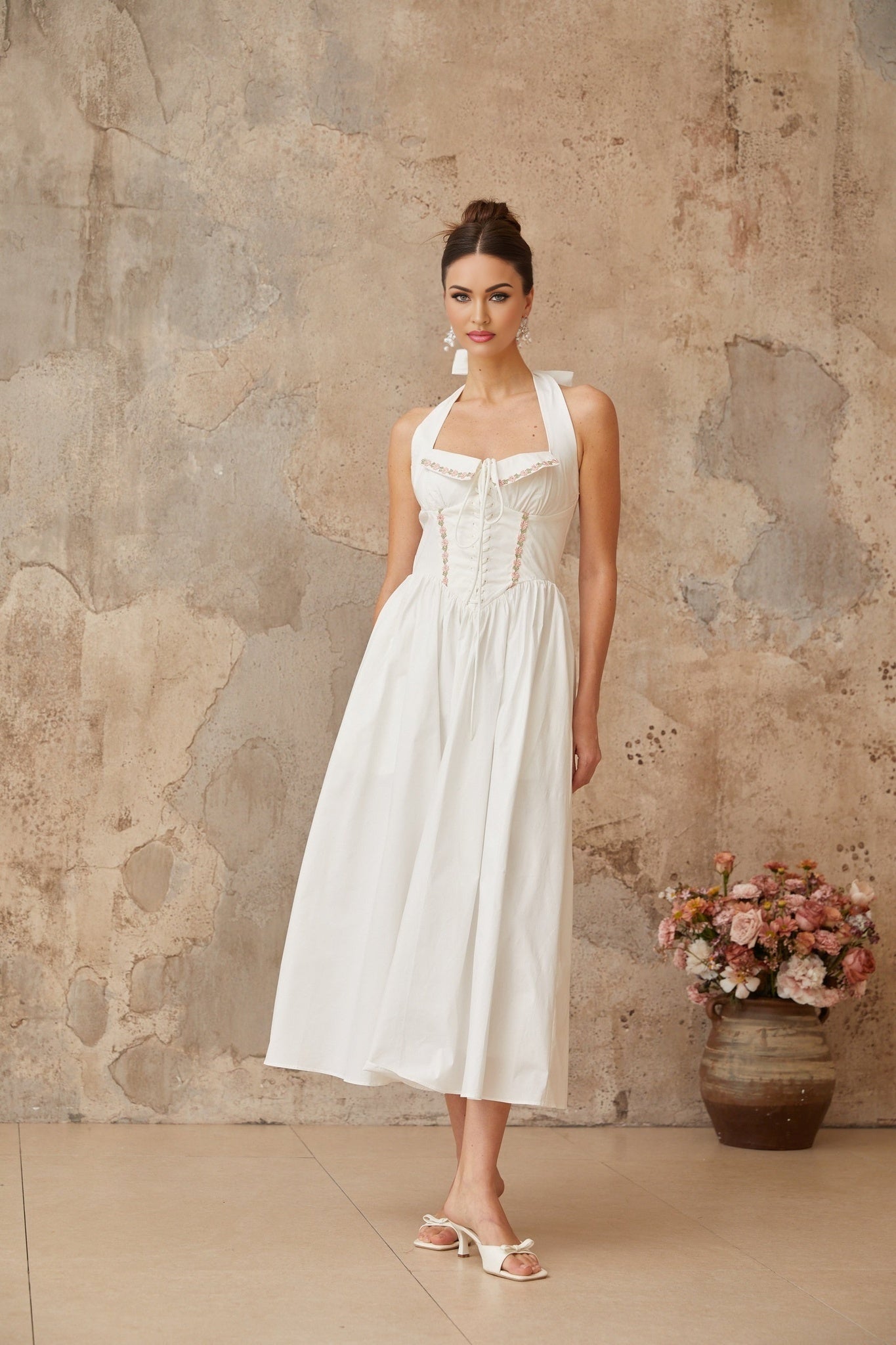 A white midi dress with laceup detailing and shirred fabric featuring a fitted bodice and flowing skirt