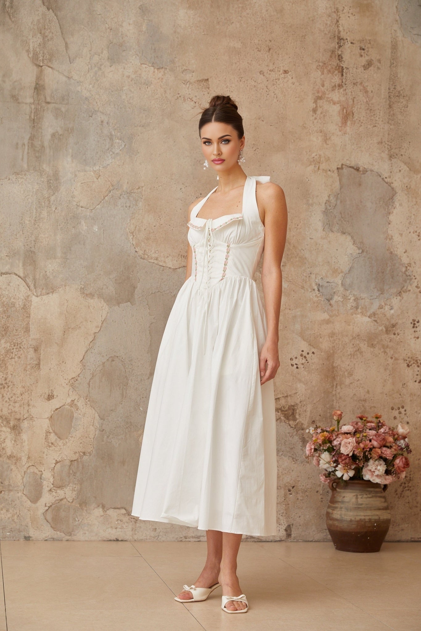 A white midi dress with laceup details and shirred fabric featuring a feminine silhouette and delicate design elements