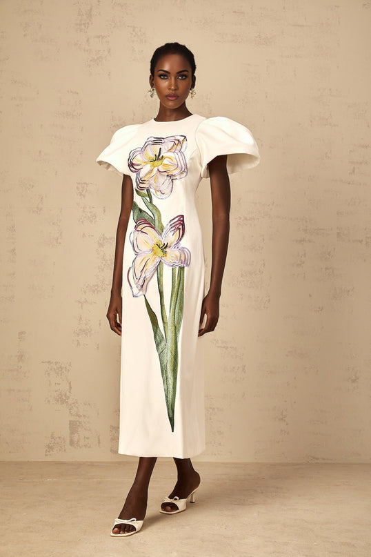 A white midi dress with sequin floral embroidery details worn by a woman standing in a neutral background