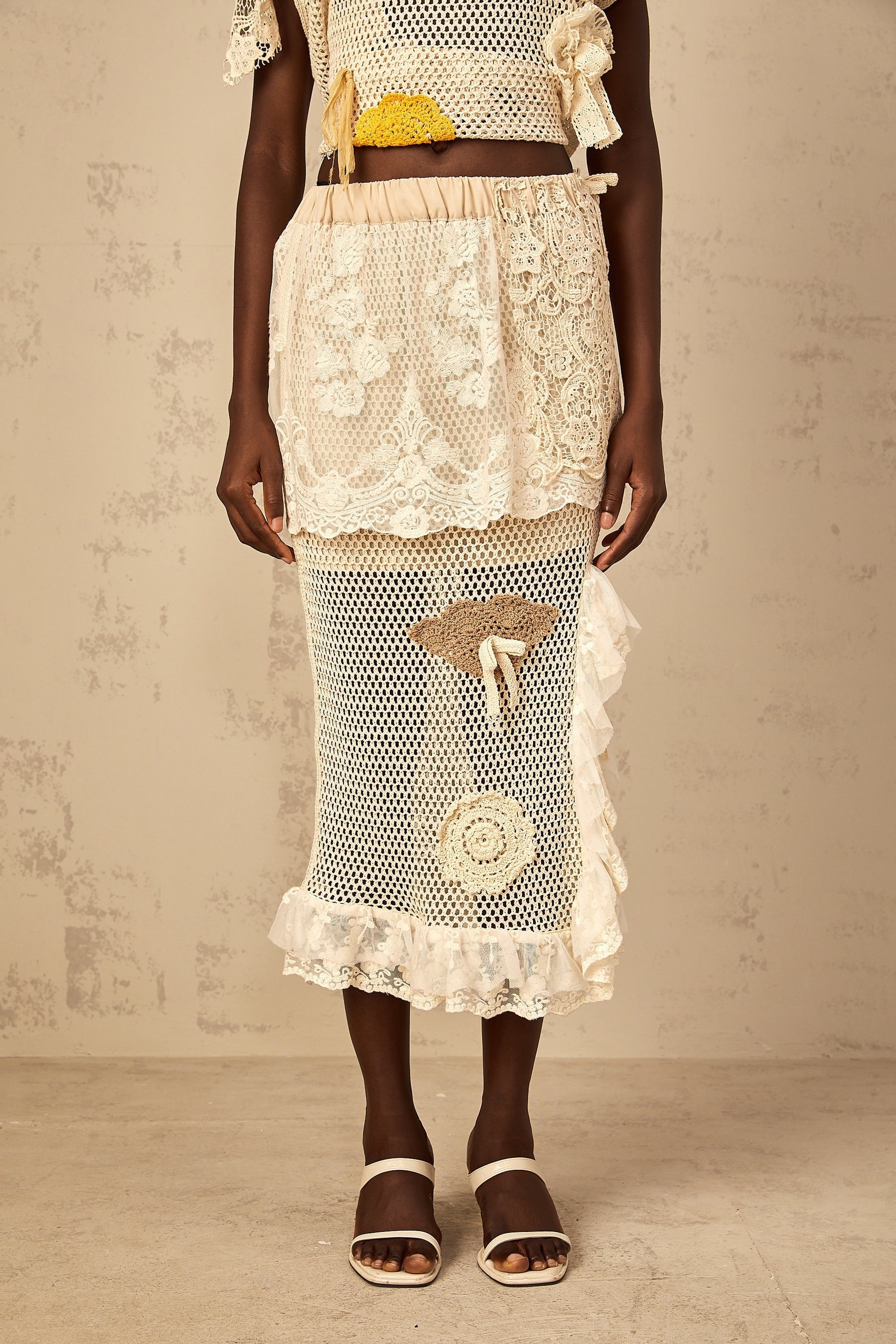 A white midi length skirt with a lace panel design and crochet knit pattern