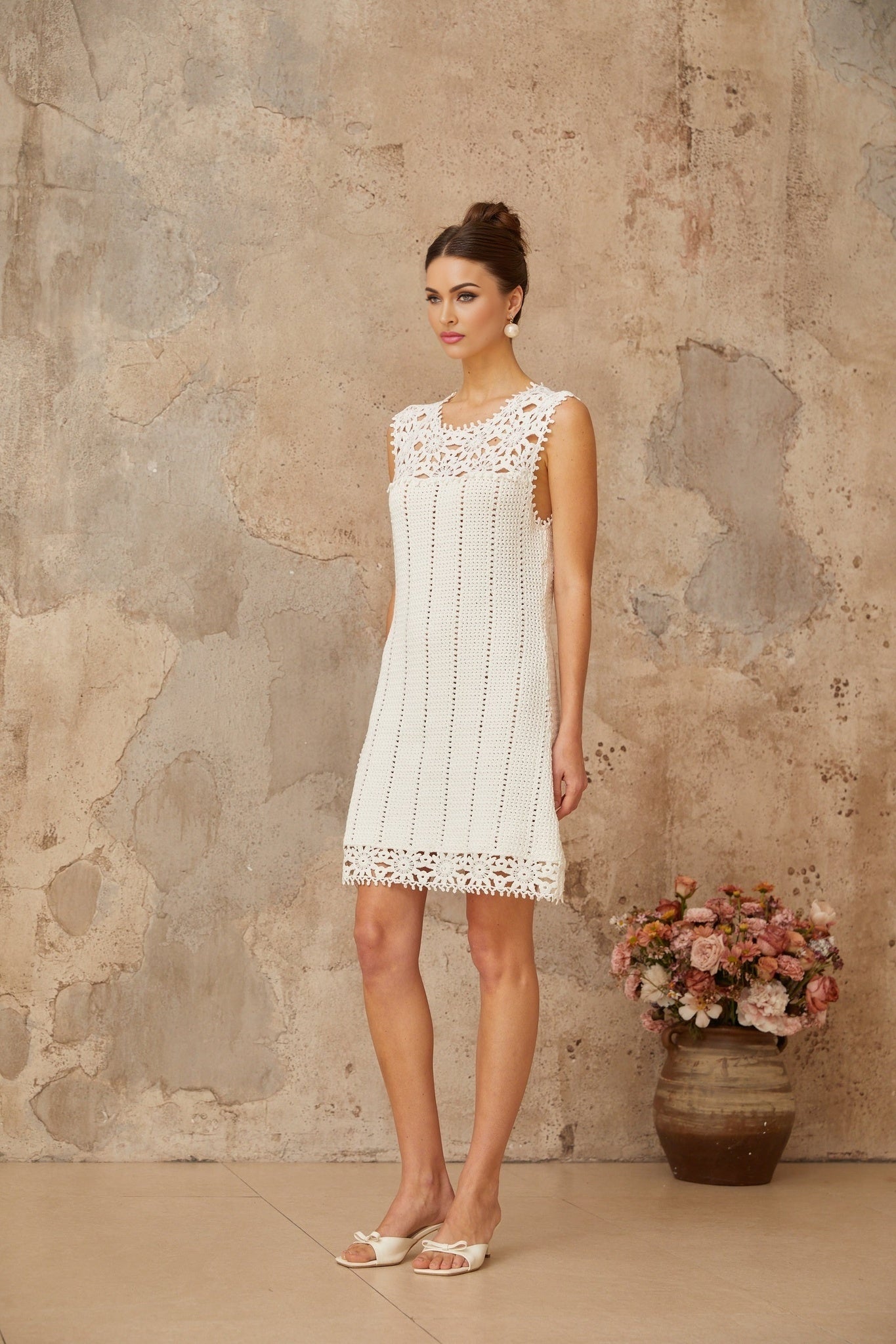 A white mini dress with a crochet knit pattern featuring floral applique details