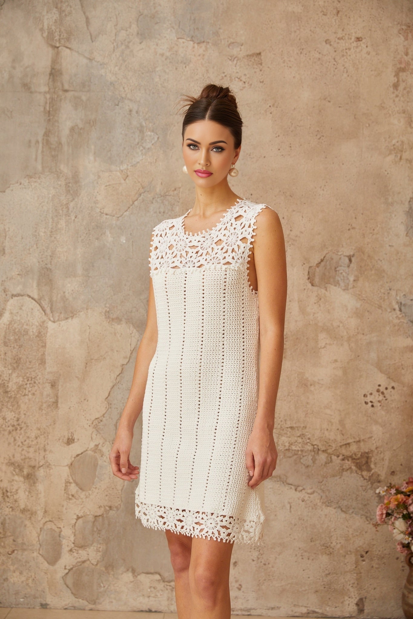 A white mini dress with a crochet knit pattern featuring floral applique details