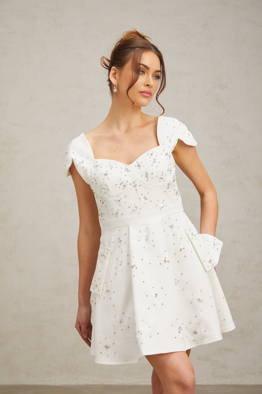 A white mini dress with a flared skirt and embellished details worn by a model named Bonnie